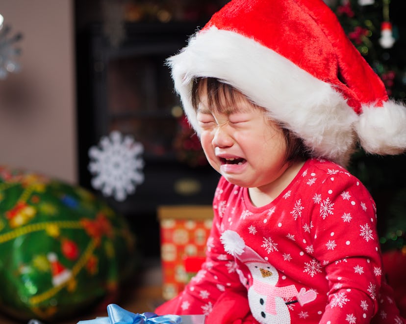 A girl crying while wearing red holiday pajamas and a red Santa cap