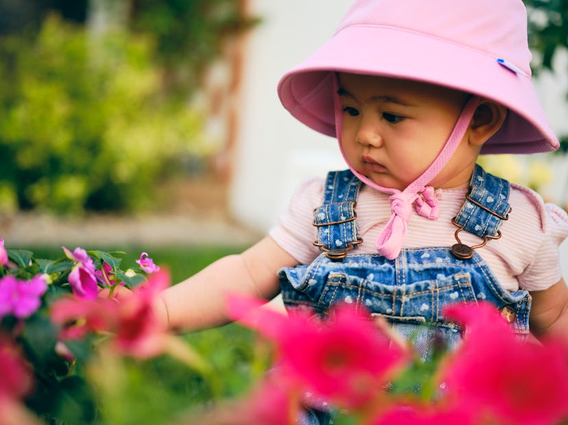 baby in pink hat looking at pink flowers for february baby names