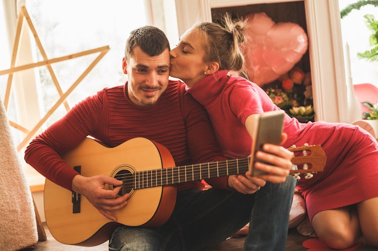 A loving couple in red and pink pose for a photo while playing the guitar on Valentine's Day.