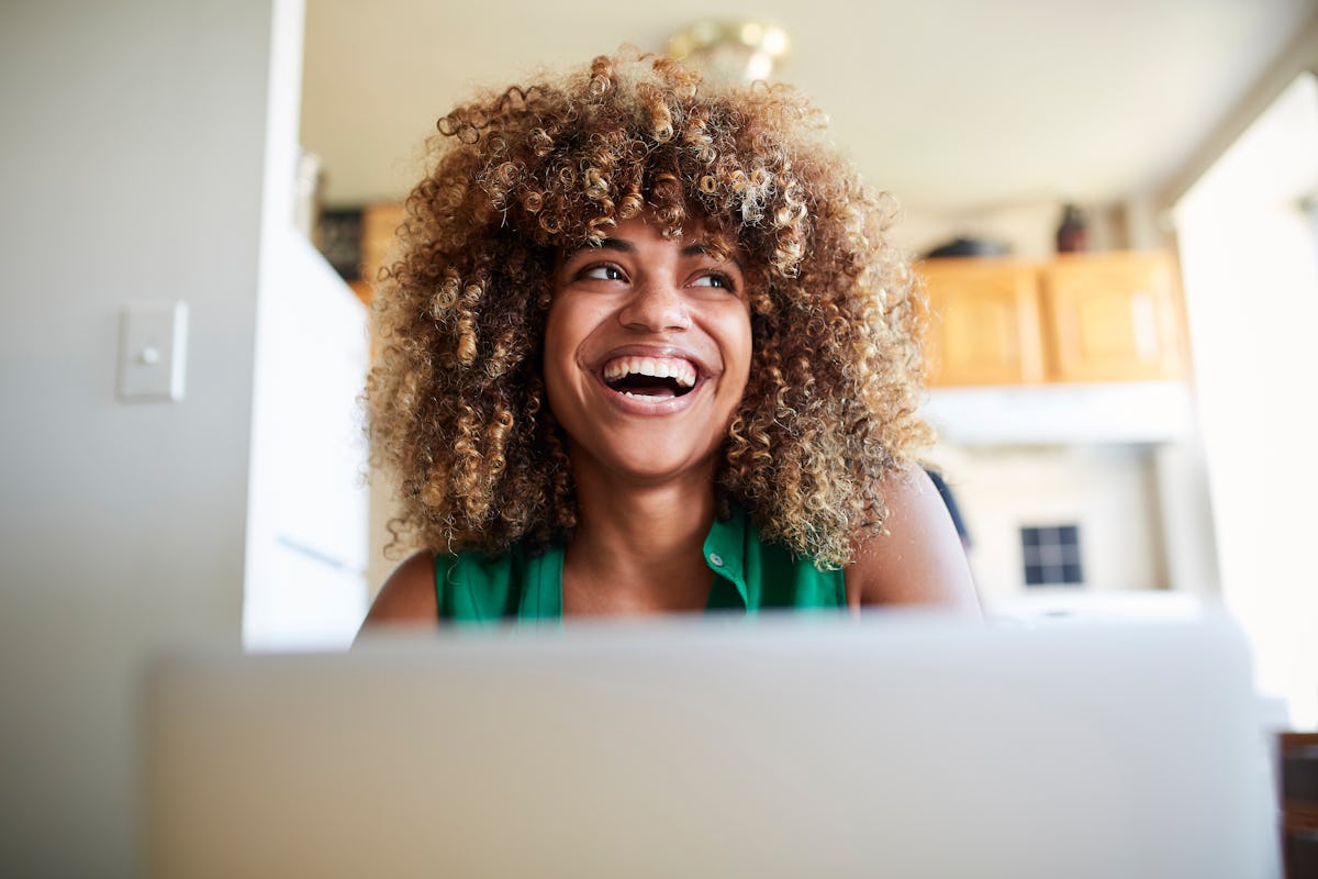 A happy woman sits at her computer at home while enjoying a virtual Galentine's Day hangout.