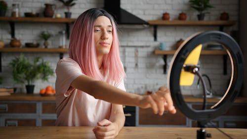 A person with pink hair records a TikTok with a ring light. The TikTok Creator Portal has resources ...