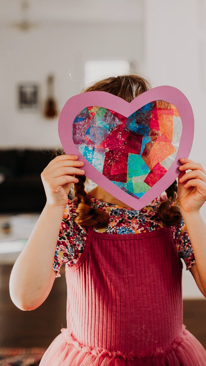 child holding up stained glass heart made from tissue paper
