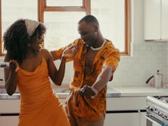 A couple in matching orange outfits dances and sings in the kitchen on Valentine's Day.