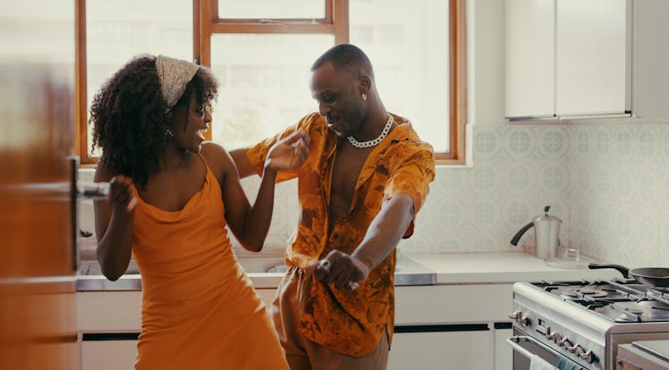 A couple in matching orange outfits dances and sings in the kitchen on Valentine's Day.