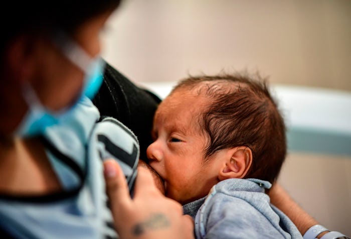 A woman breastfeeds an infant while wearing a face mask.