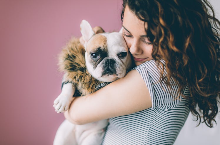 A woman holds her dog in front of a pink wall for Valentine's Day.