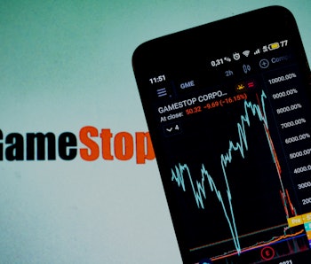 A stock exchange chart is seen in the background. A smartphone shows the GameStop shares chart.
