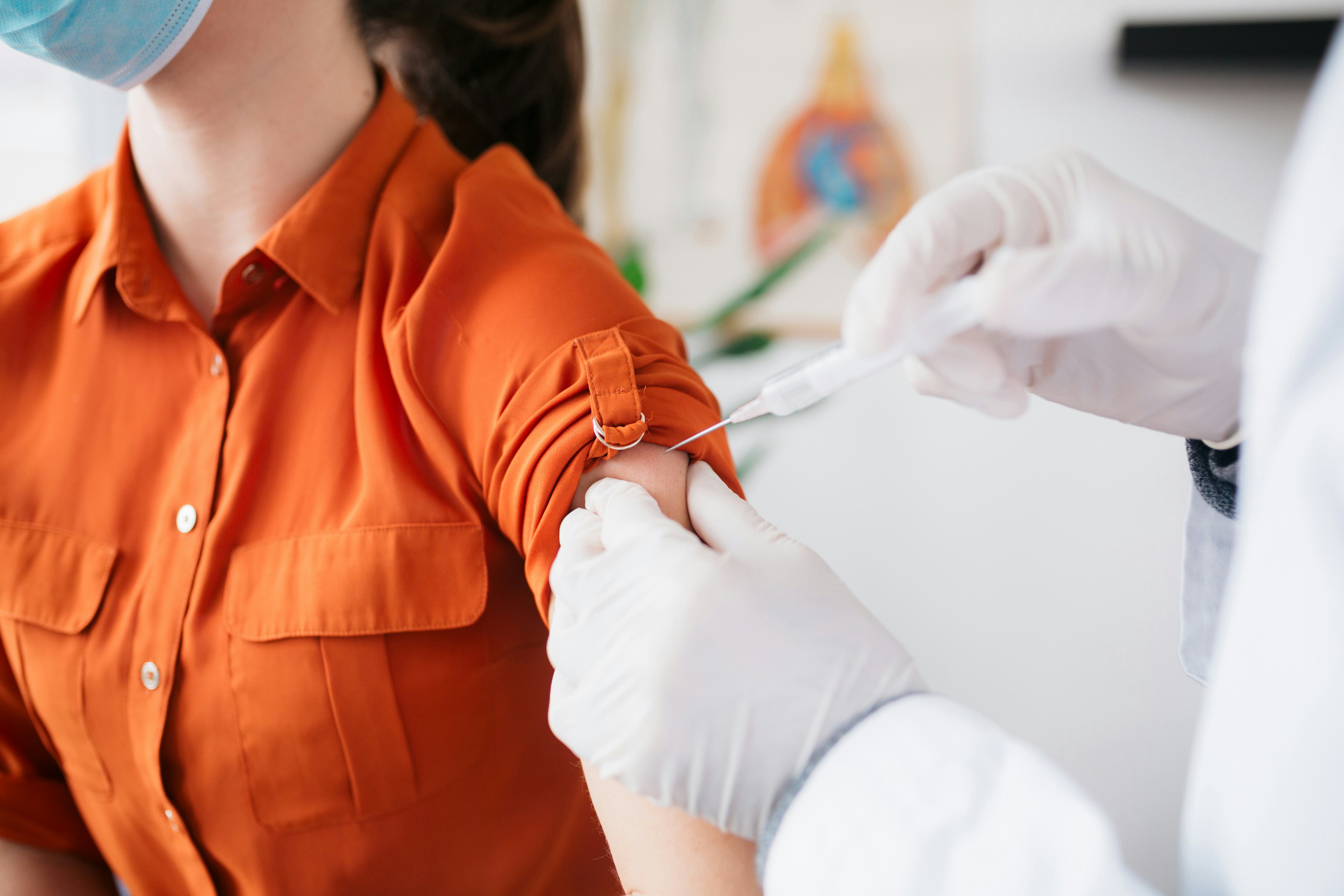 A woman wearing an orange shirt receives the COVID vaccine.
