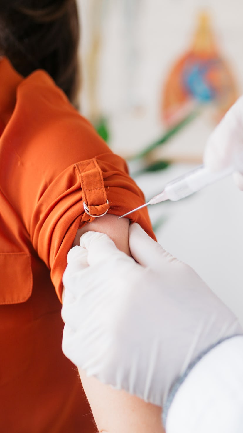 A woman wearing an orange shirt receives the COVID vaccine.