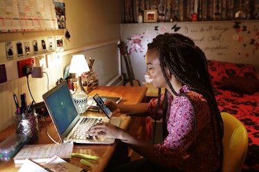 A young woman plays on her phone, while sitting at her desk in a decorated bedroom.