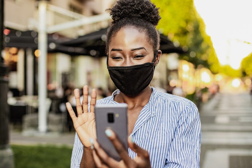 A woman in a mask waves hi to a person she recognizes via facetime.