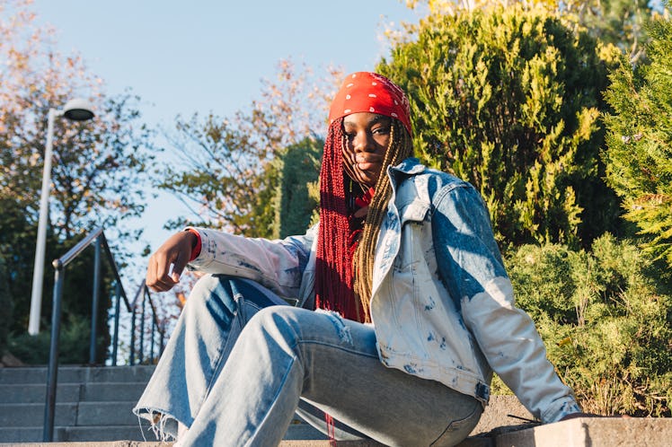 A young woman poses in flared jeans and a denim jacket while sitting in her local park.
