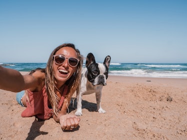 A happy woman takes a selfie with her dog at the beach. 