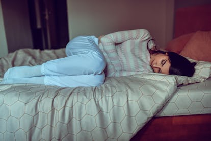 Uma mulher esfrega o estômago enquanto está deitada na cama. Gessos decíduais podem ser sinais de gravidezes ectópicas.