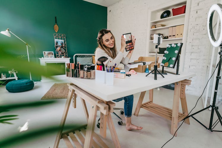 A young woman poses with a makeup palette while filming the emoji makeup challenge for TikTok.