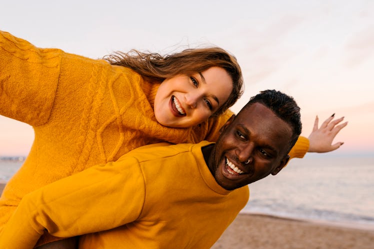 A happy woman sits on her partner's back on the beach.