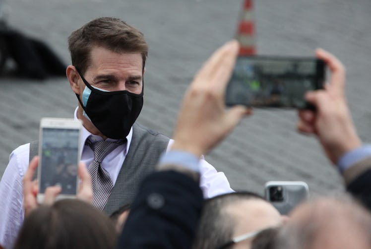Tom Cruise wearing a face mask in front of fans, who are holding up two smartphones as cameras.