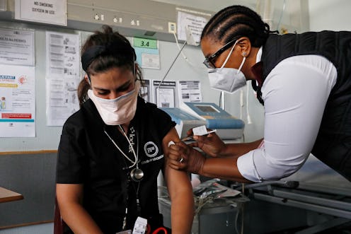 A person wears a mask while giving someone a COVID vaccine shot in the left arm. Knowing what to do ...