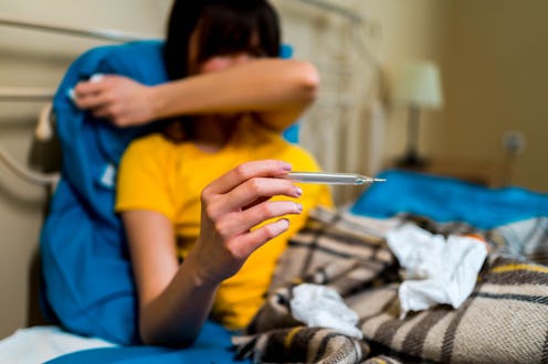 A person sneezes into their elbow while holding a thermometer in their other hand. Having a fever is...