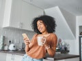 A young woman looks at coffee hacks on TikTok on her phone while drinking coffee in her minimalistic...