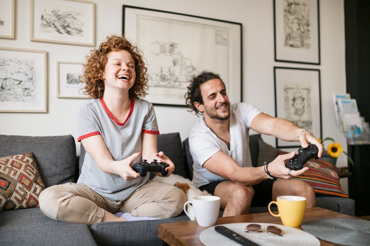 A young couple plays video games and laughs while sitting on their couch.