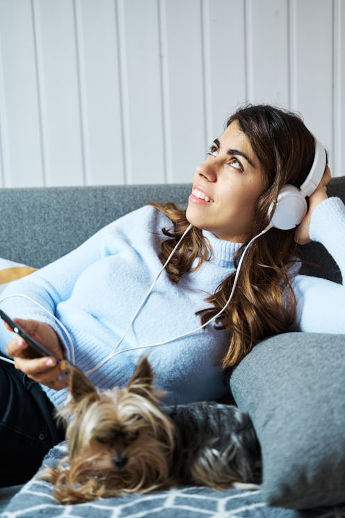 A woman with headphones listens to a room on Clubhouse next to her dog. Clubhouse is a great place t...