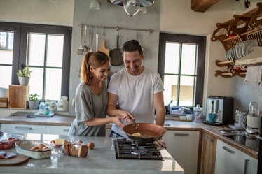 A happy couple fries an egg to make egg sandwiches in their bright kitchen.