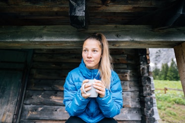 A young woman enjoys a hot cup of tea while wearing a bright blue puffer jacket in the outdoors.