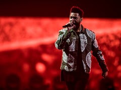 The Weeknd sings on stage in front of a glowing red backdrop.