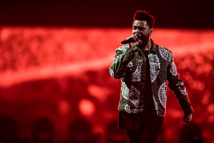 The Weeknd sings on stage in front of a glowing red backdrop.