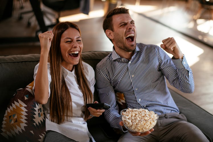 A young couple cheers while eating popcorn and watching the Super Bowl 2021 Halftime Show.