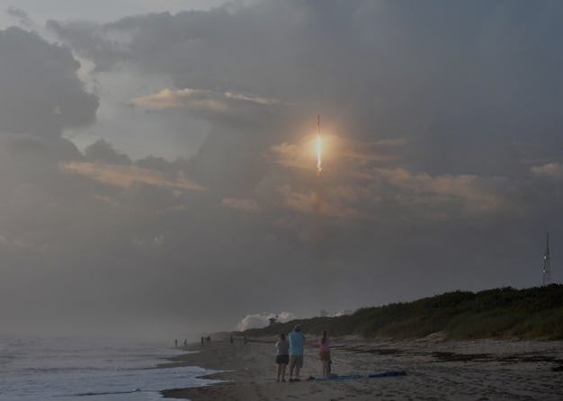 People on a beach watching a rocket fly into the atmosphere.
