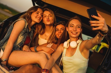 A group of friends pose for a selfie in the trunk of their car at sunset while on a road trip.