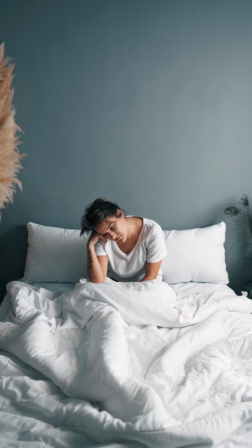 A woman lies in bed next to pampas grass, experiencing fatigue after a mild covid case turned into l...