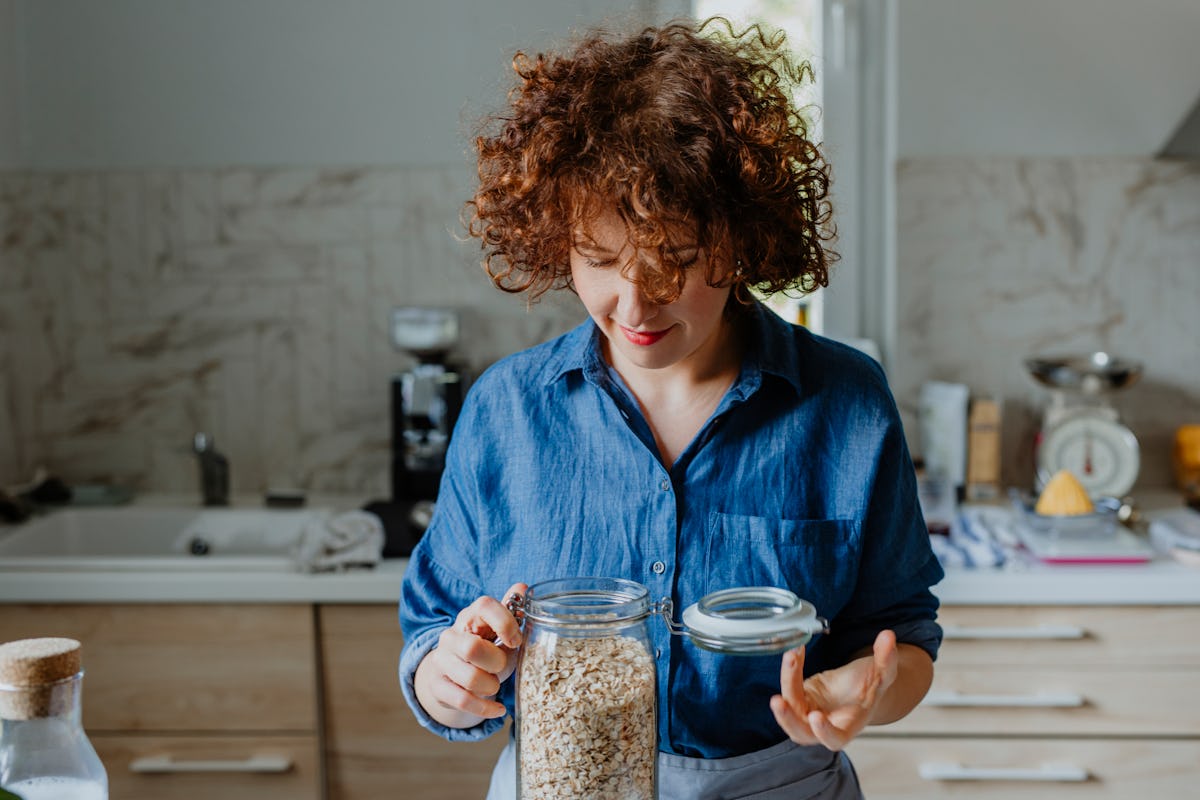 A woman looks into a jar of oats in her kitchen.