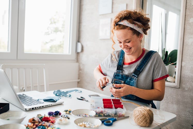 A smiling woman crafts a necklace using string, beads, and charms.