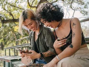 Two sisters laugh while looking at their phone. 