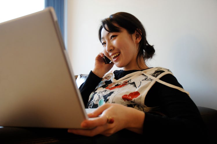 A young woman talks on the phone while holding her laptop.