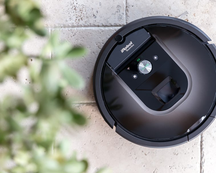 An iRobot Roomba is seen placed near a bush.