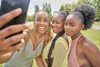 Three sister pose for a picture together on their phone while outside. 