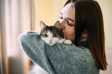 A woman kisses her cat on its head while holding it. 