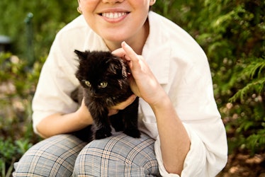 A woman holds a little black kitten, while sitting outside. 