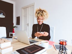 A young woman texts her study group while doing homework and drinking coffee at her kitchen table.