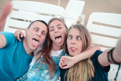 Three siblings make funny faces while posing for a selfie on their phone. 