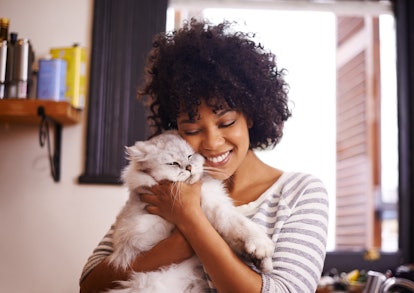 A happy woman hugs her fluffy white cat at home. 