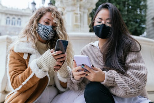 Two people wearing masks and looking at their phones wondering how the new COVID-19 variants are dif...