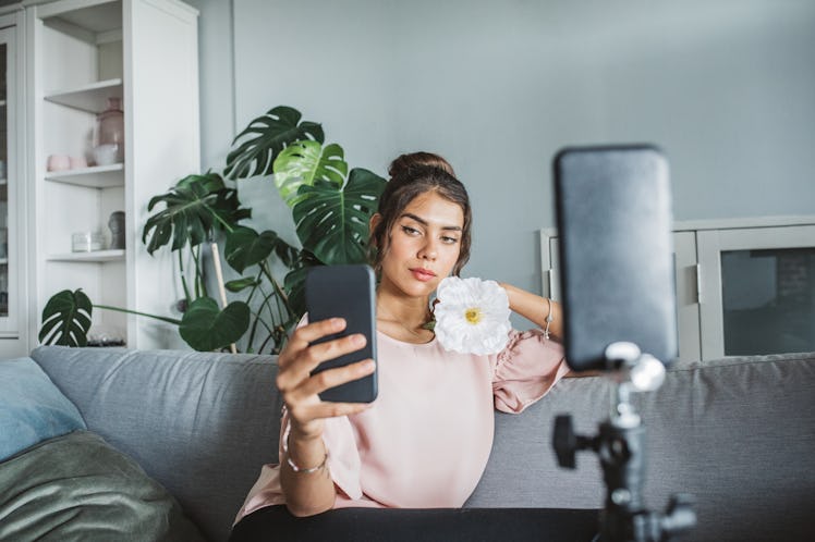 A young woman takes a selfie with a flower, while sitting on her couch during spring break.