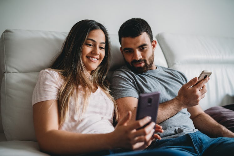 A couple relaxes on a couch and smiles while texting in a couples group chat.