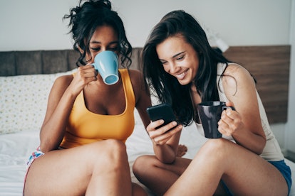 A happy couple enjoys coffee while sitting on their bed and texting in their couples group chat.