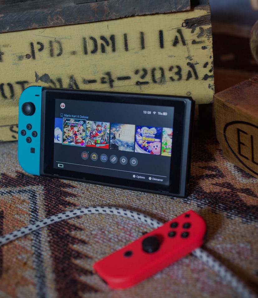 A Nintendo Switch Lite can be seen on a surface with a wooden box behind it.